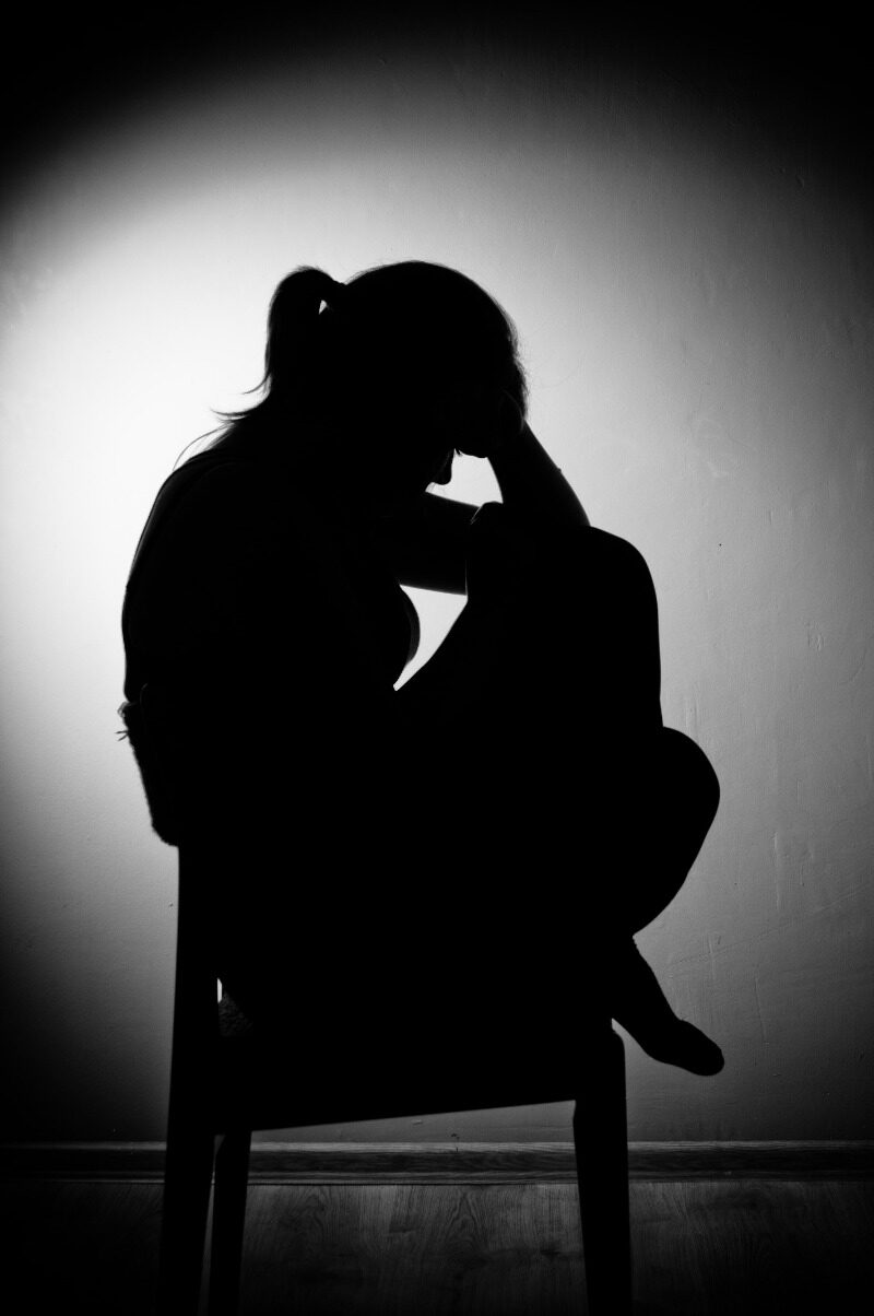 Silhouet van een vrouw die in een stoel zit met haar hoofd in haar handen, illustrerend het ongemak en de schaamte van Persistent Genital Arousal Disorder (PGAD)